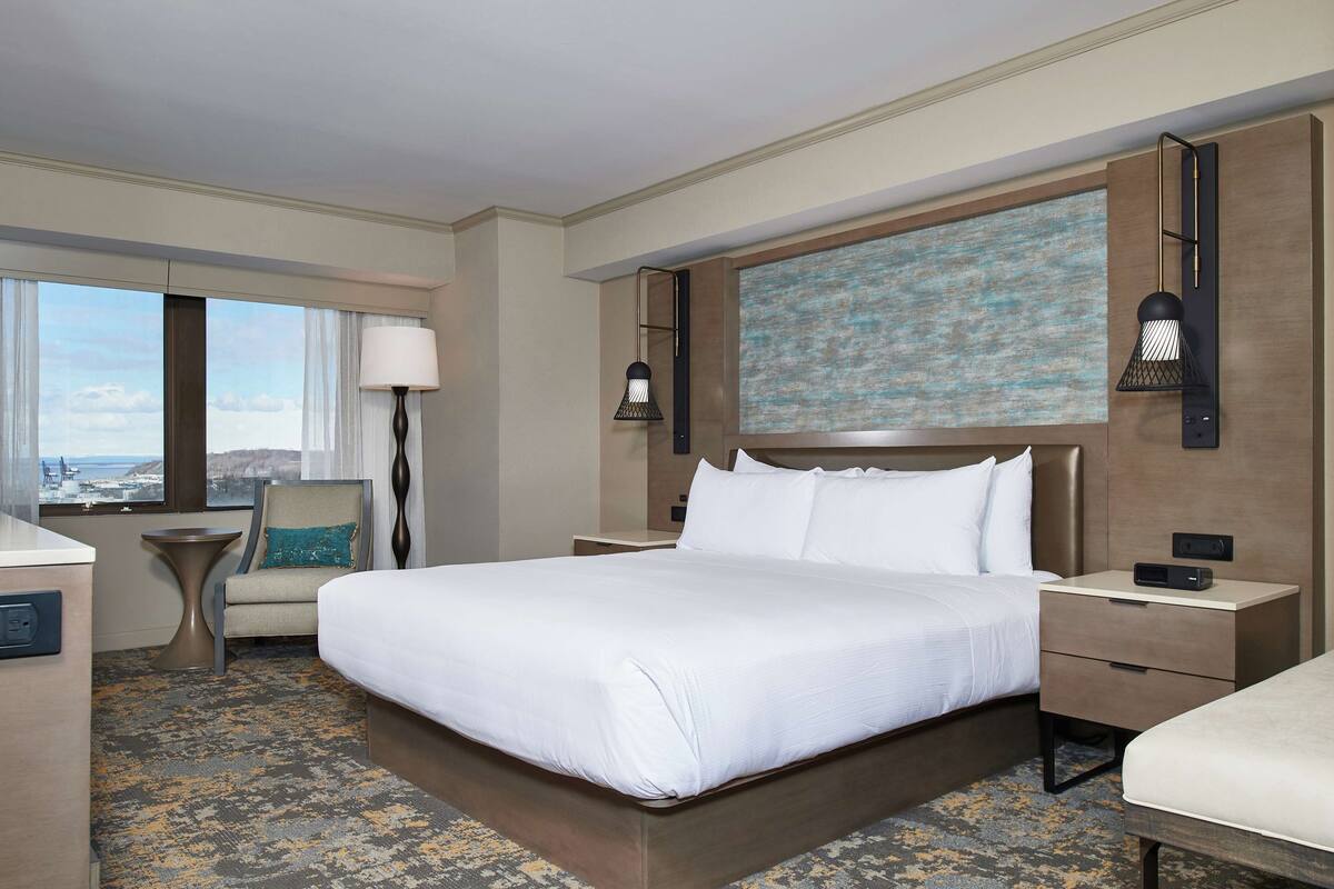 A hotel room with a large bed, a desk, a chair, and a view of the city.