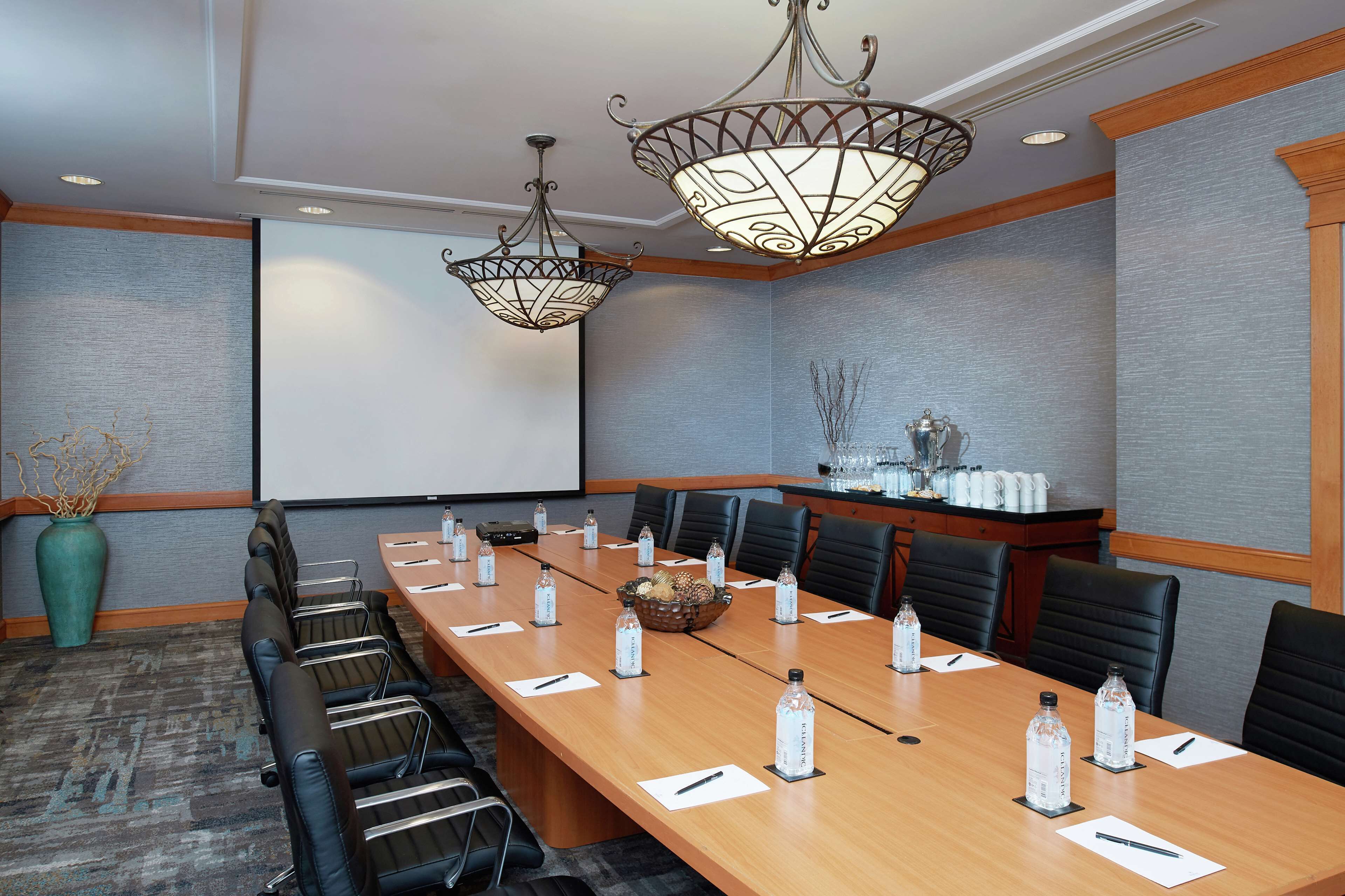 A conference room with a long table, black chairs, and a projector screen.