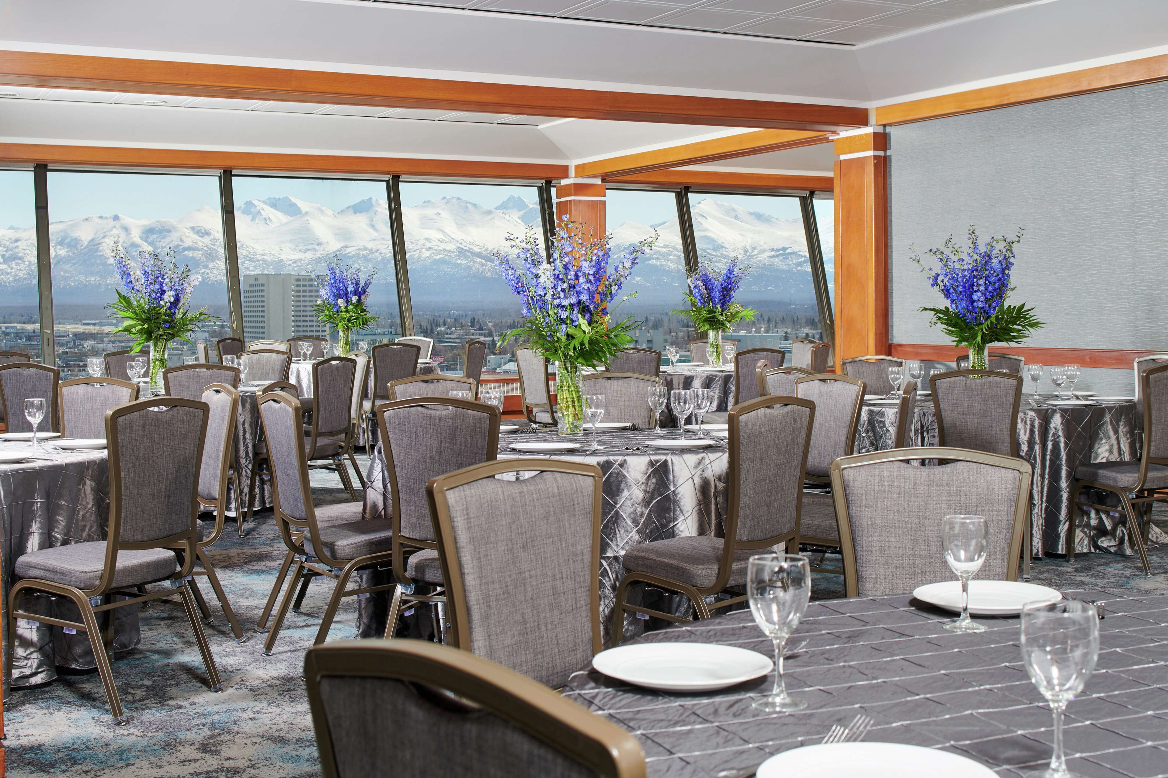 Ein Konferenzraum mit Tischen und Stühlen, großen Fenstern mit Blick auf Berge und floralen Tischdekorationen.