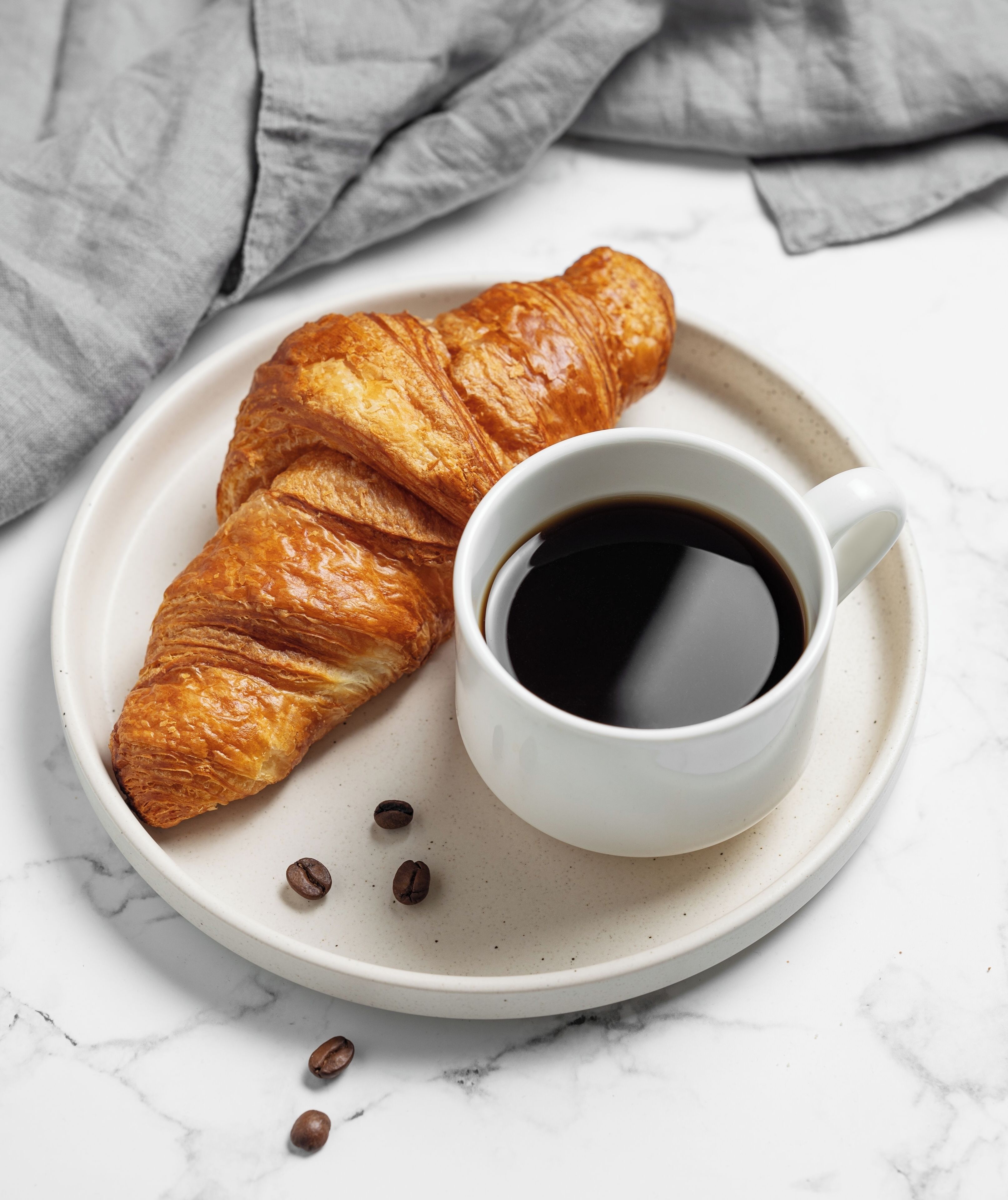 A croissant and a cup of coffee on a plate.