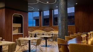 Un comedor moderno con paredes de madera, ventanas amplias y una mezcla de sillas de metal y tapizadas.
