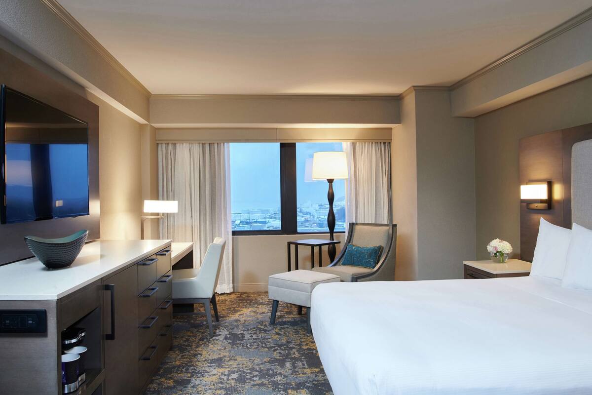 A hotel room with a bed, a desk, a chair, a small table, and a window with curtains.