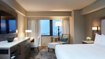 A hotel room with a bed, a desk, a chair, a small table, and a window with curtains.