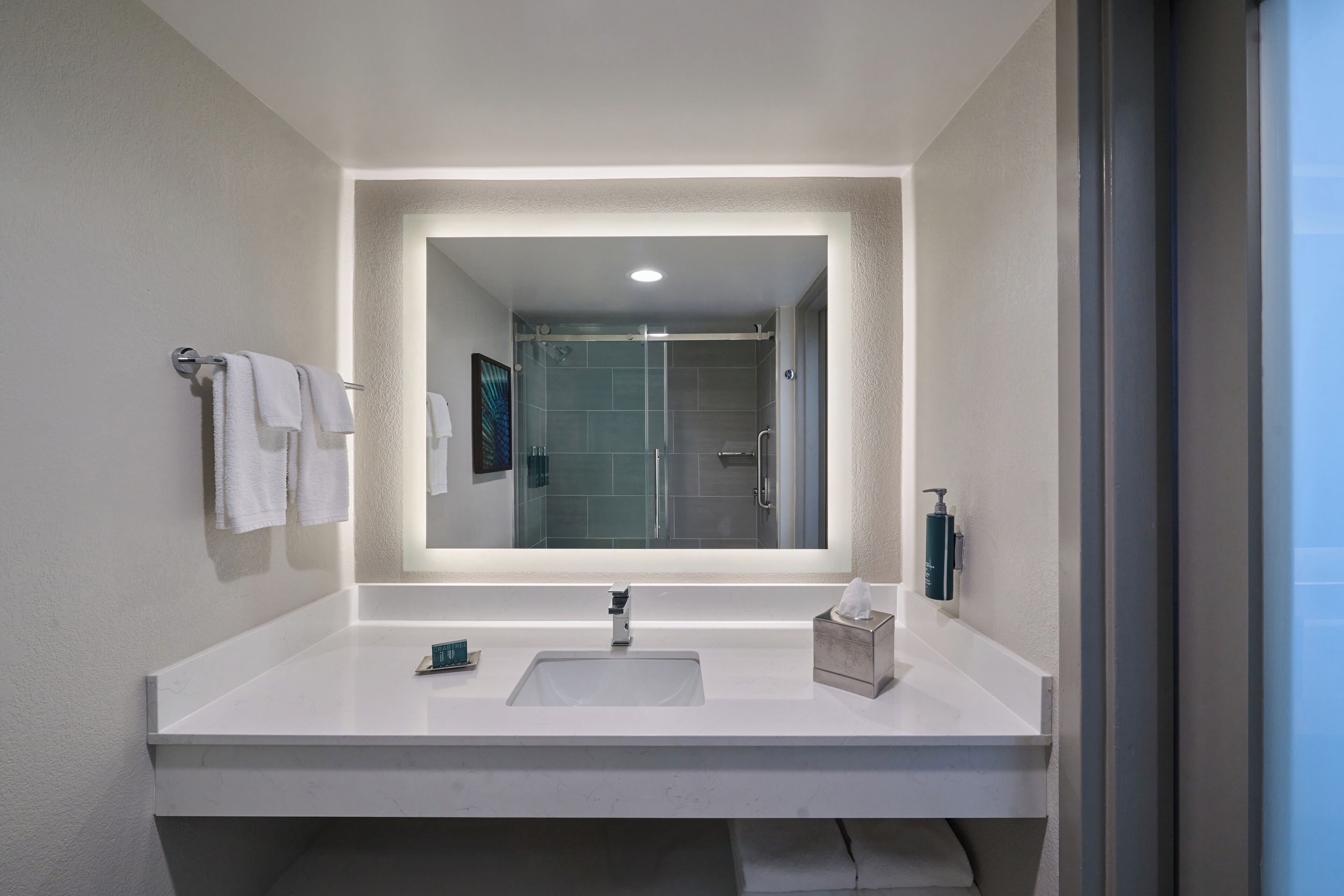 A modern bathroom with a large mirror, two sinks, and a shower visible in the background.