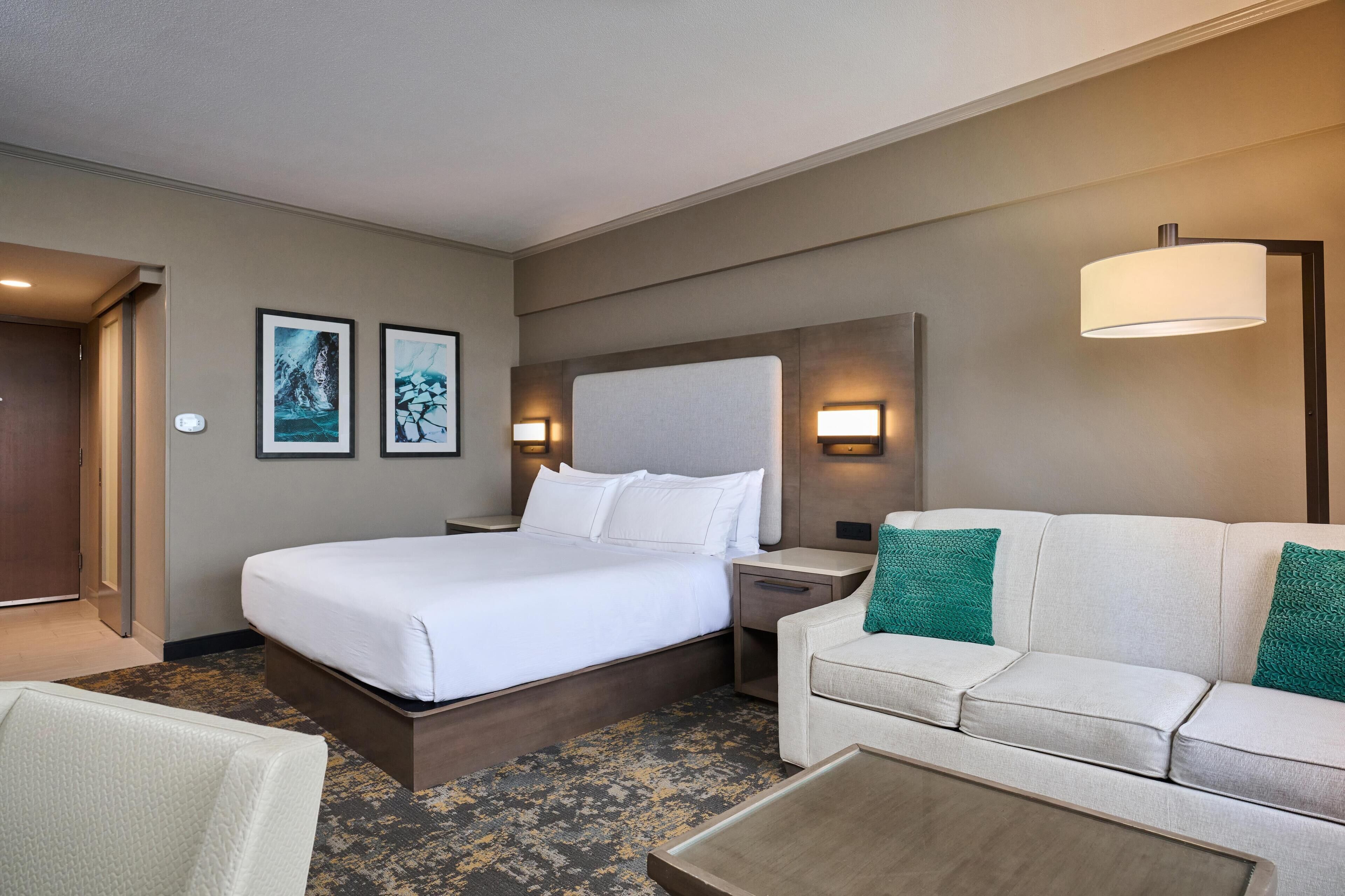 A hotel room with a bed, a sofa, a coffee table, and two wall-mounted lamps.