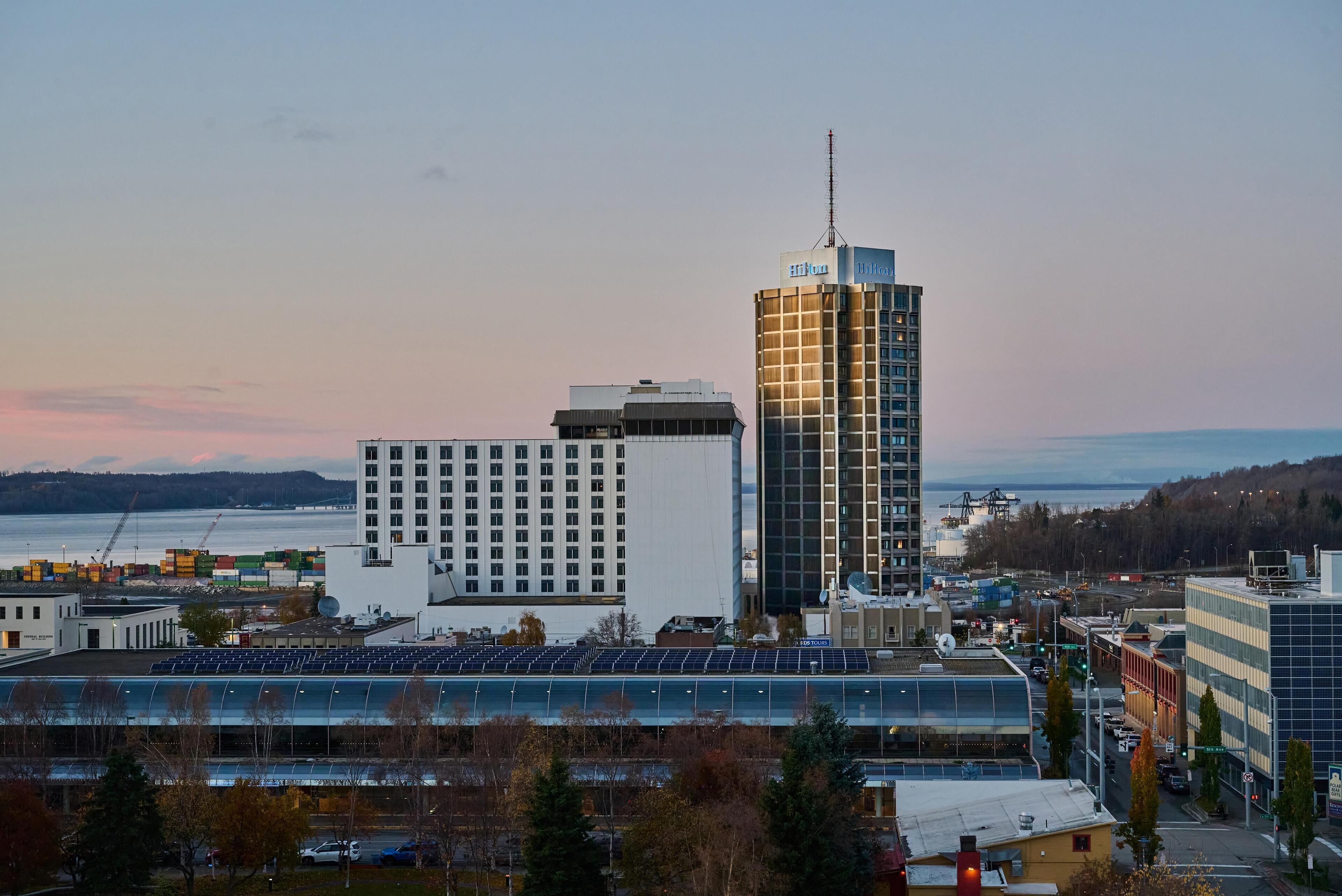 A high-rise hotel with a modern design, located near a waterfront with visible shipping containers and a solar panel array.