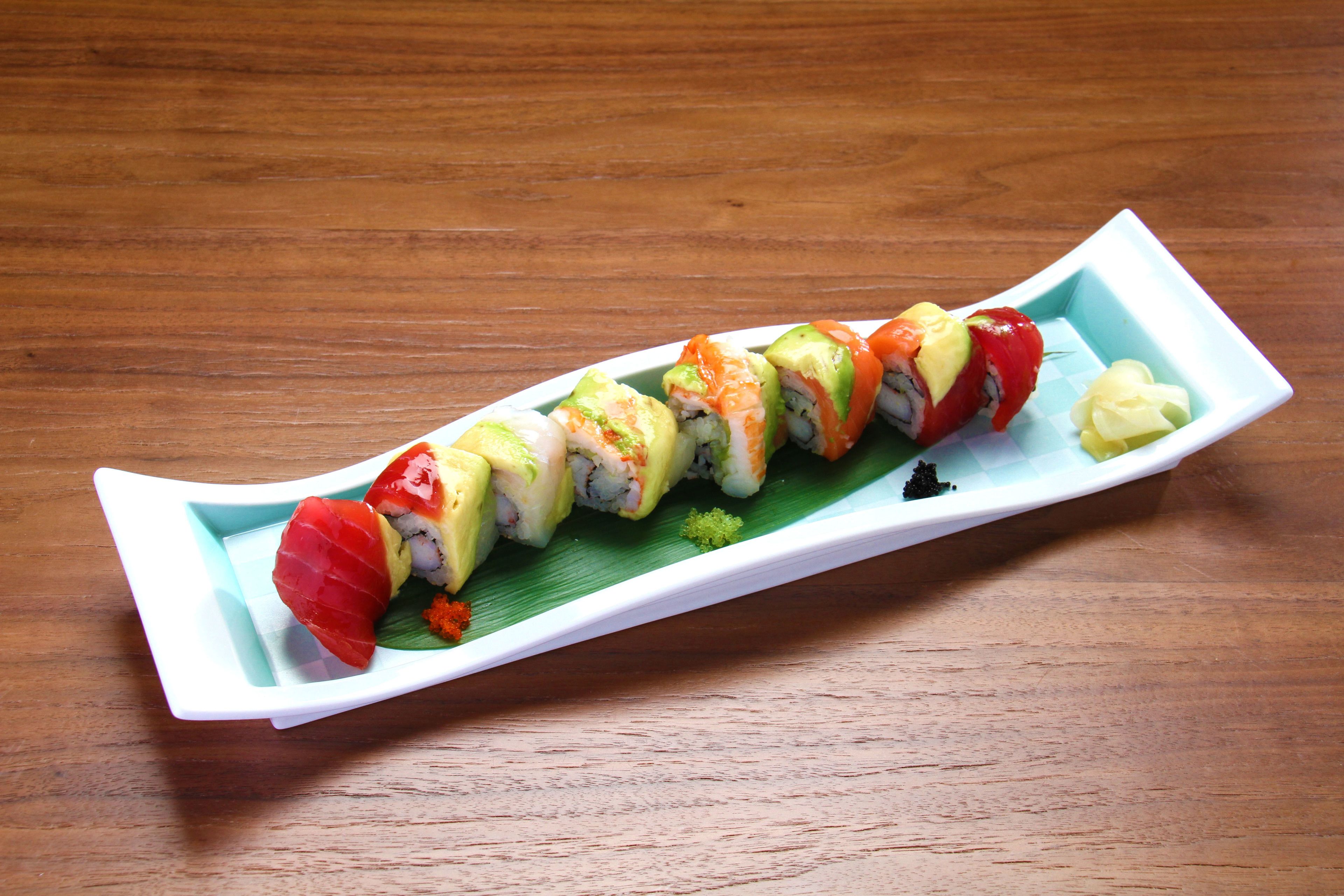 A sushi platter on a white rectangular plate with a green leaf garnish, placed on a wooden table.
