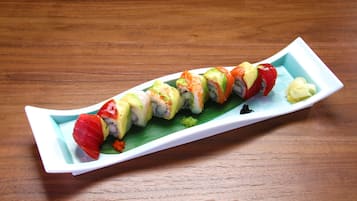A sushi platter on a white rectangular plate with a green leaf garnish, placed on a wooden table.
