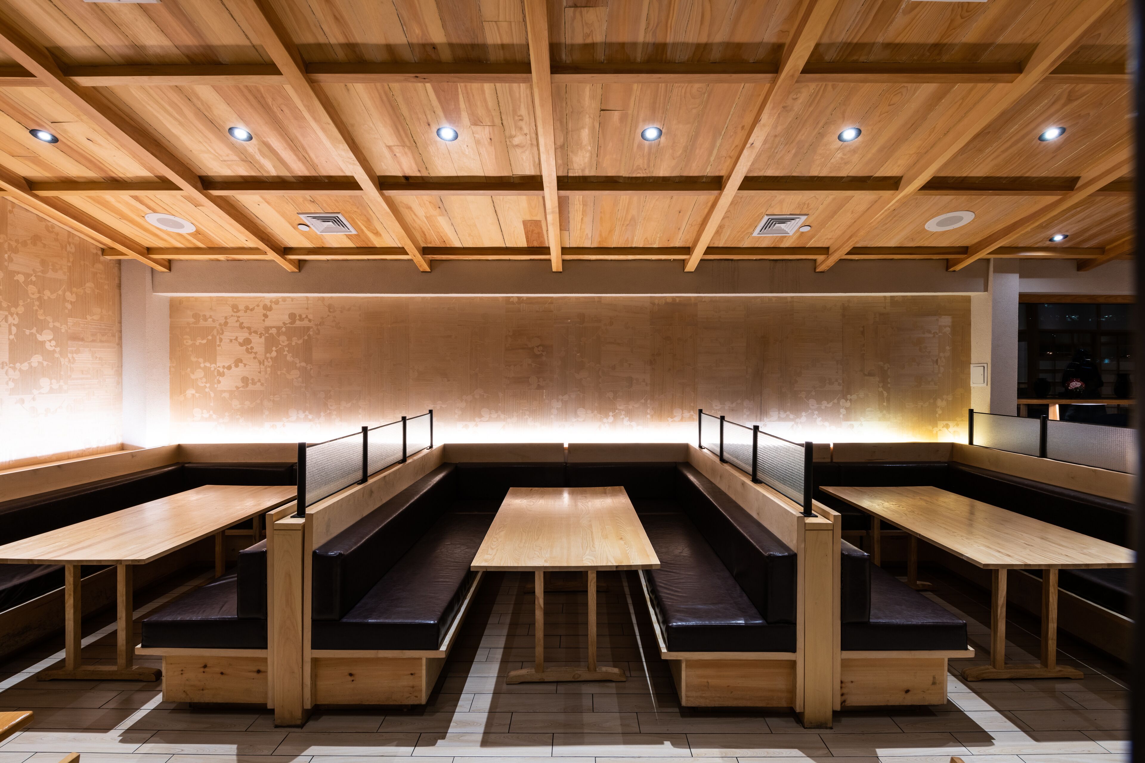 A restaurant with wooden benches and tables, a high ceiling with exposed beams, and recessed lighting.