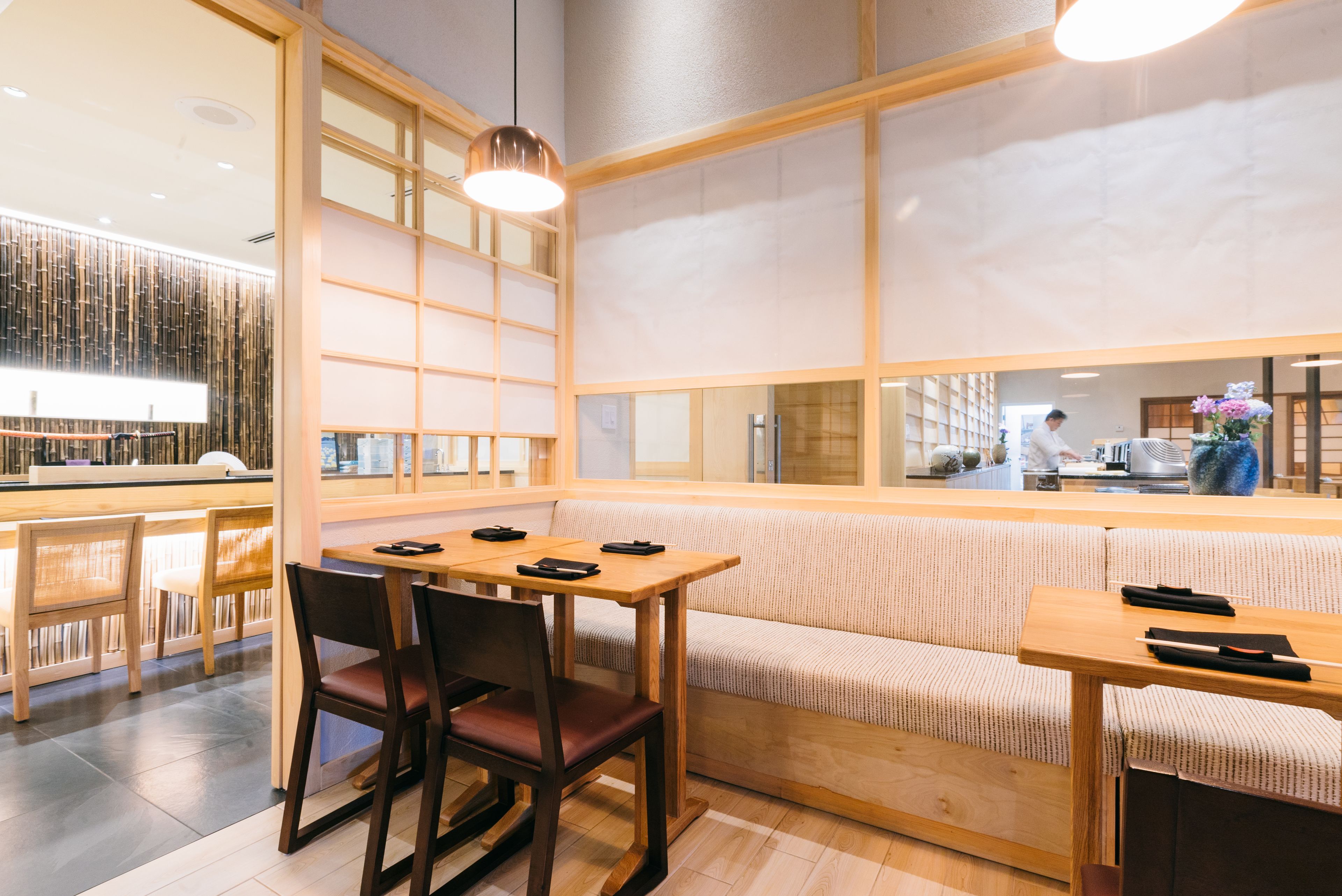 Um interior moderno com uma mesa e cadeiras de madeira, um banco acolchoado e vista através de uma grande janela.