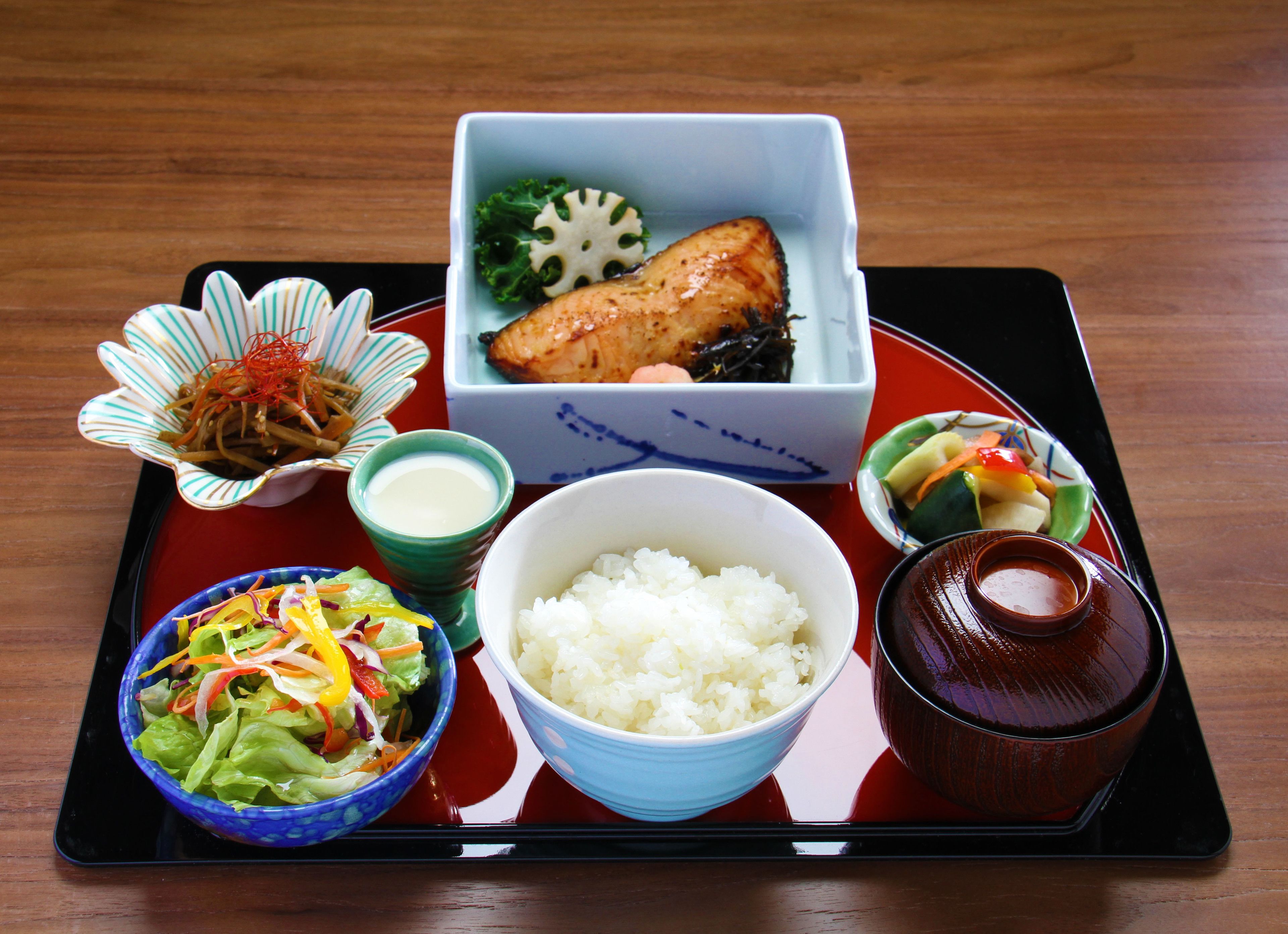 A tray with a variety of Japanese dishes including rice, fish, salad, and a small bowl of soup.