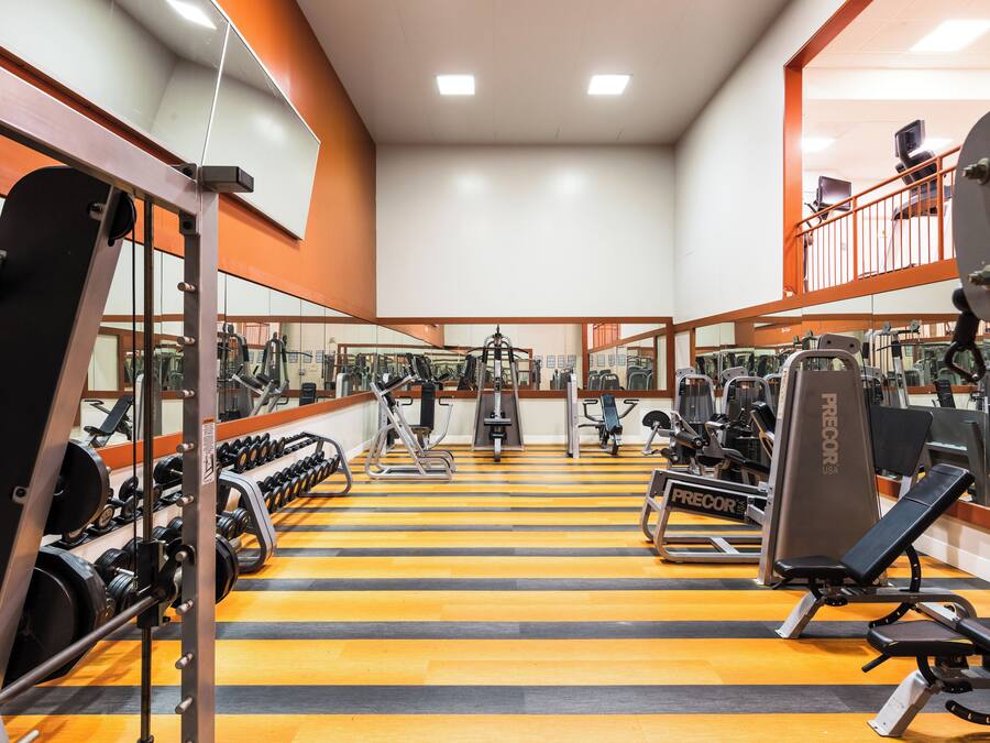 A gym with various exercise equipment, mirrors, and a yellow-striped floor.
