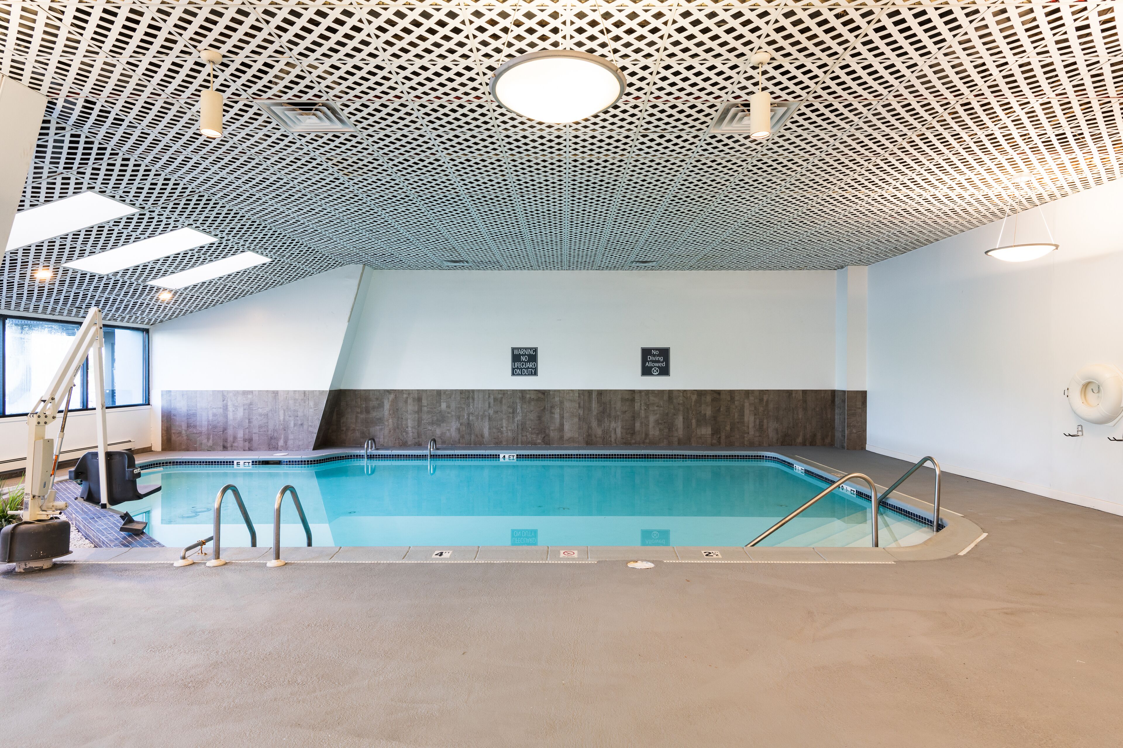Ein Innenpool mit modernem Deckenbau, deutlich markiertem Poolbereich und einem sichtbaren Rettungsschwimmerstuhl.
