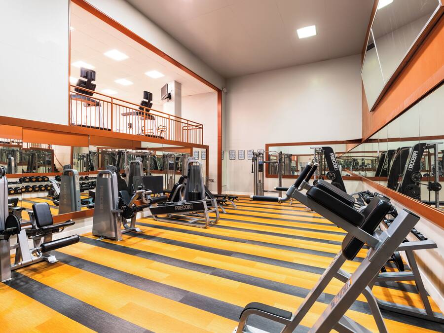 Una palestra con diverse attrezzature per esercizi, pareti a specchio e pavimento in legno.