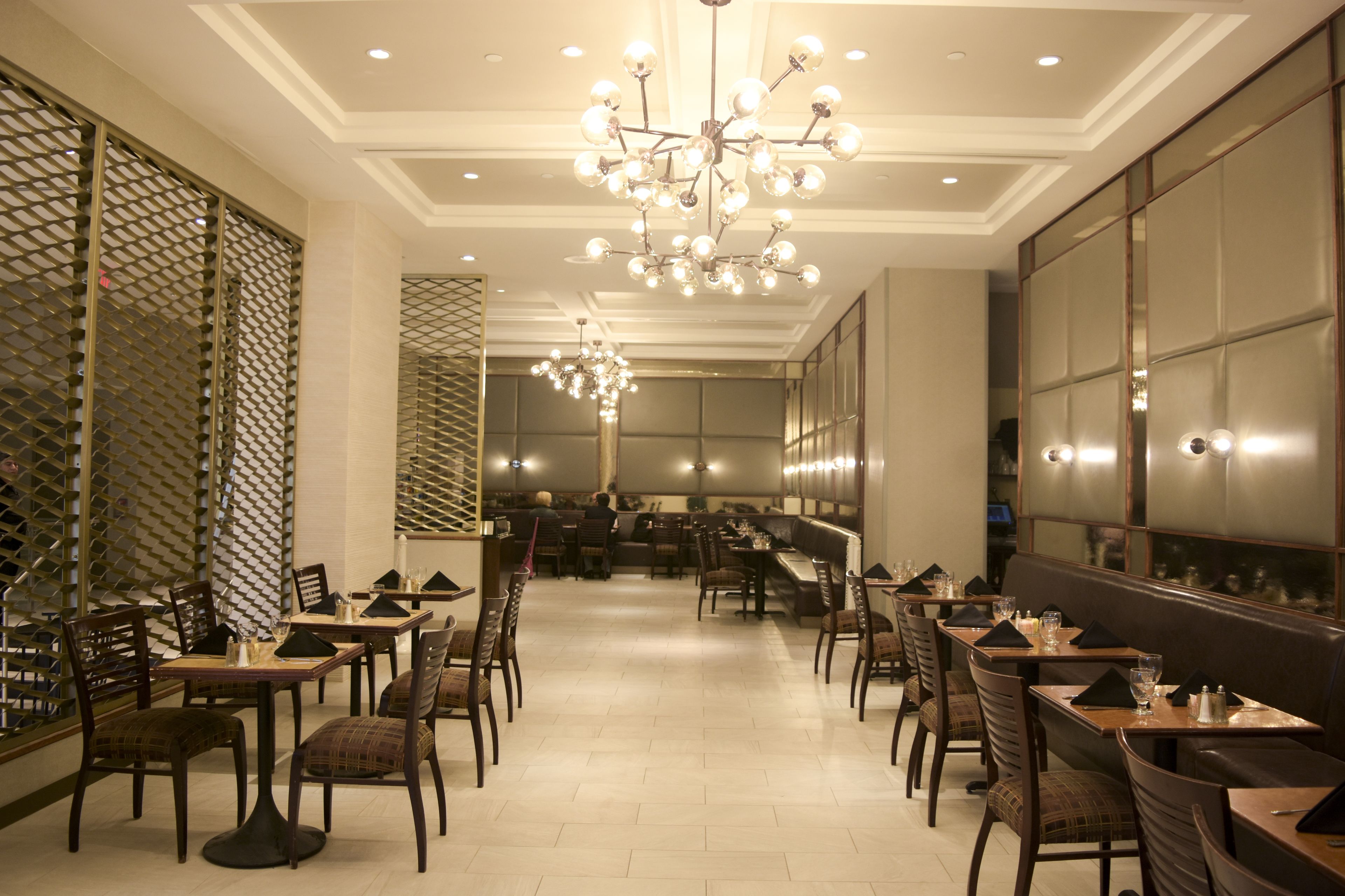 A spacious restaurant with multiple dining tables and chairs, a central chandelier, and a modern interior design.