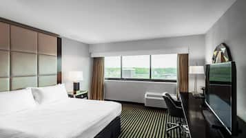 A hotel room with a large bed, a desk with a chair, a television, and a window with a city view.