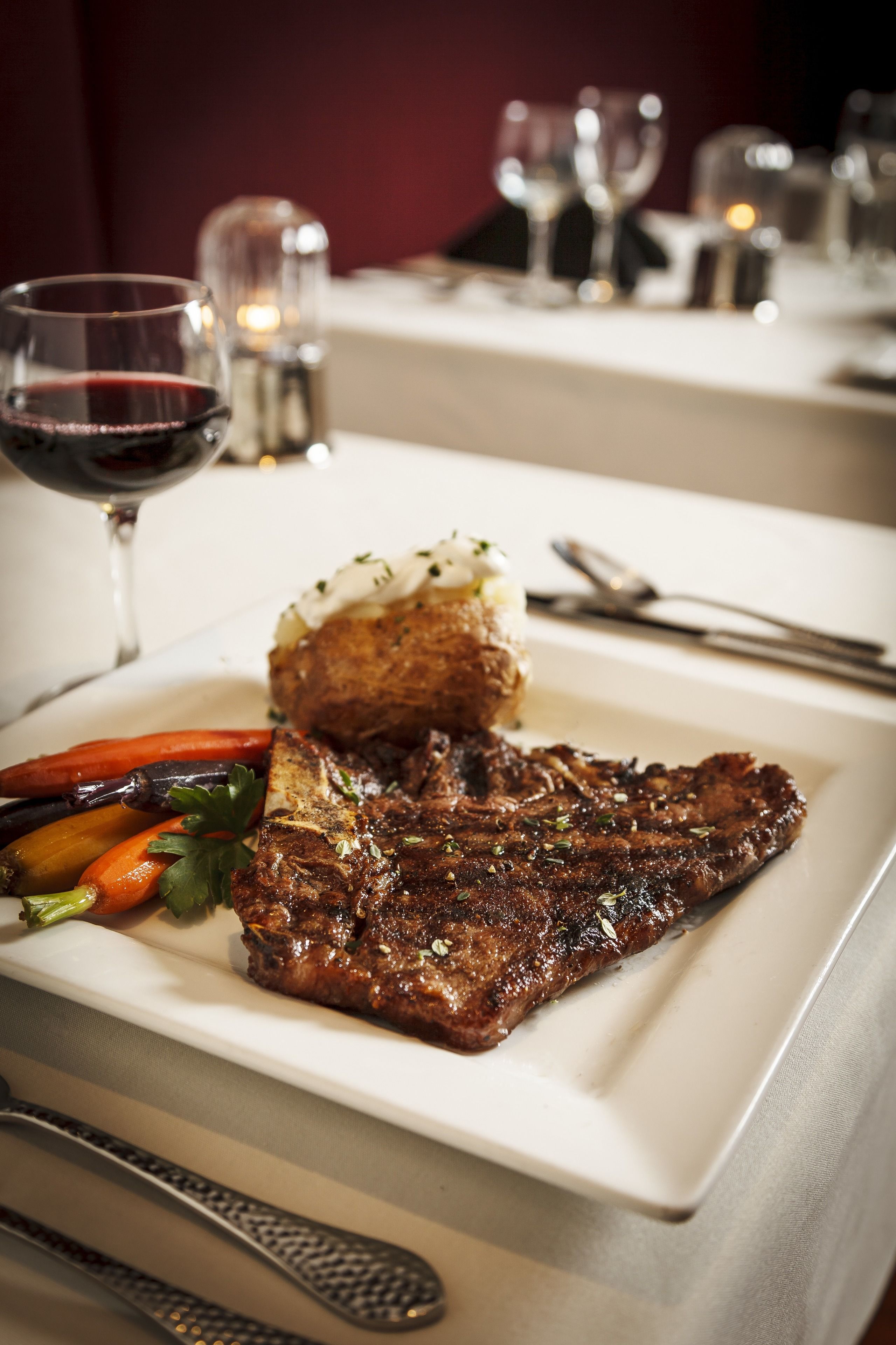Un steak accompagné de légumes et d’un accompagnement, le tout servi dans une assiette, avec un verre de vin rouge.