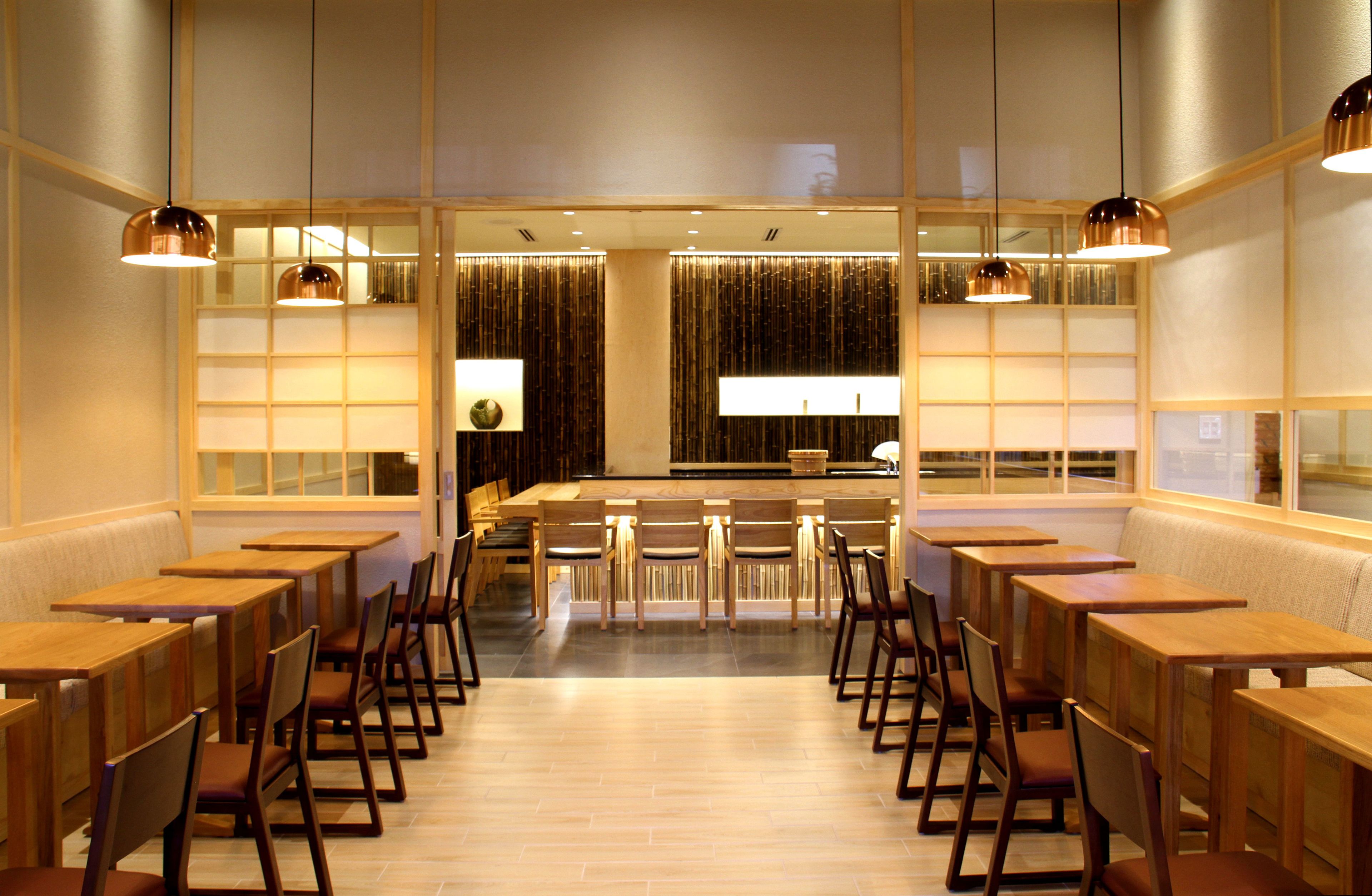 Un restaurante con mesas y sillas de madera, una zona de bar central e iluminación colgante.