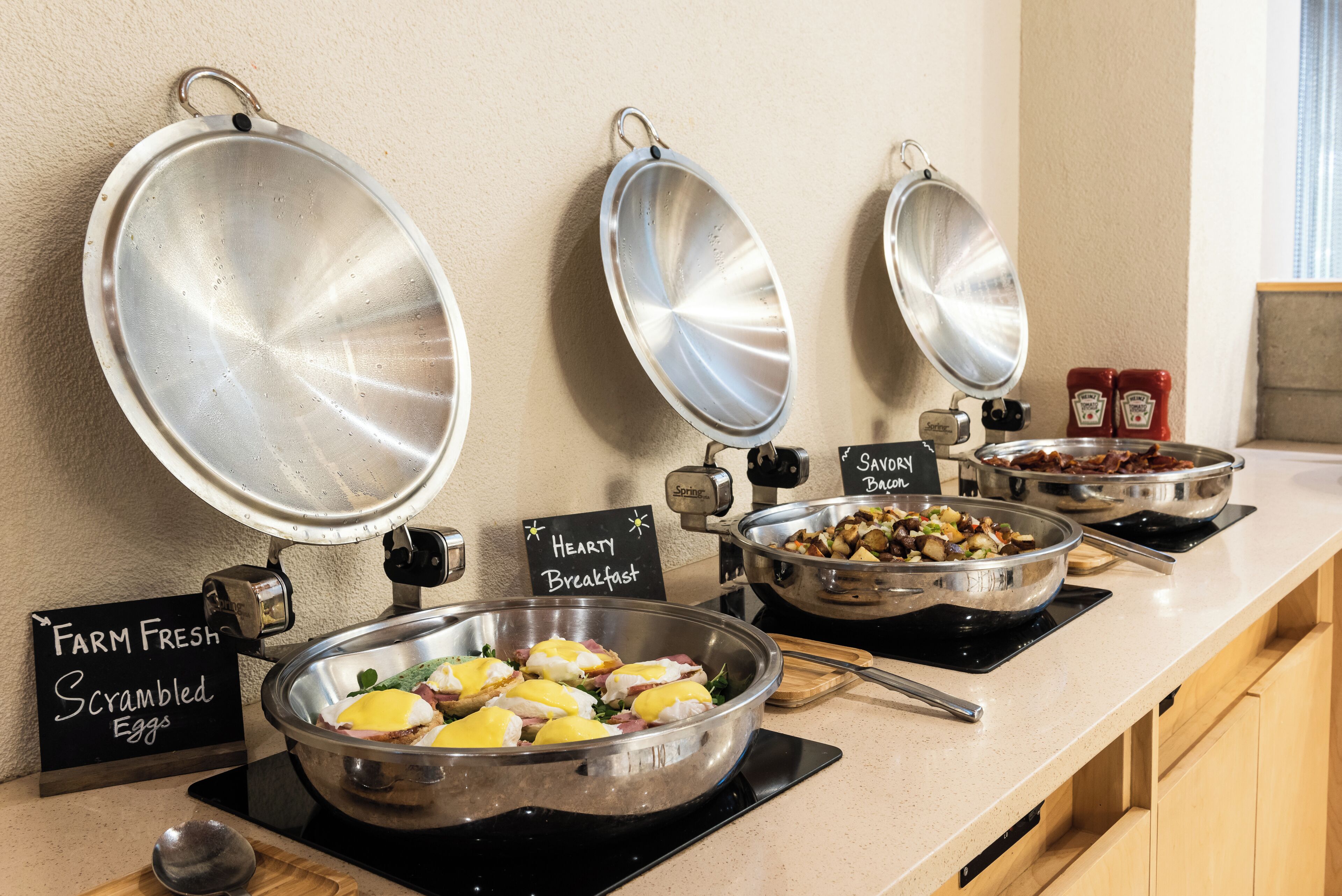 Ein reichhaltiges Frühstücksbuffet mit gekennzeichneten Speisen, darunter Rührei, ein herzhaftes Frühstück und schmackhaftes Speck.