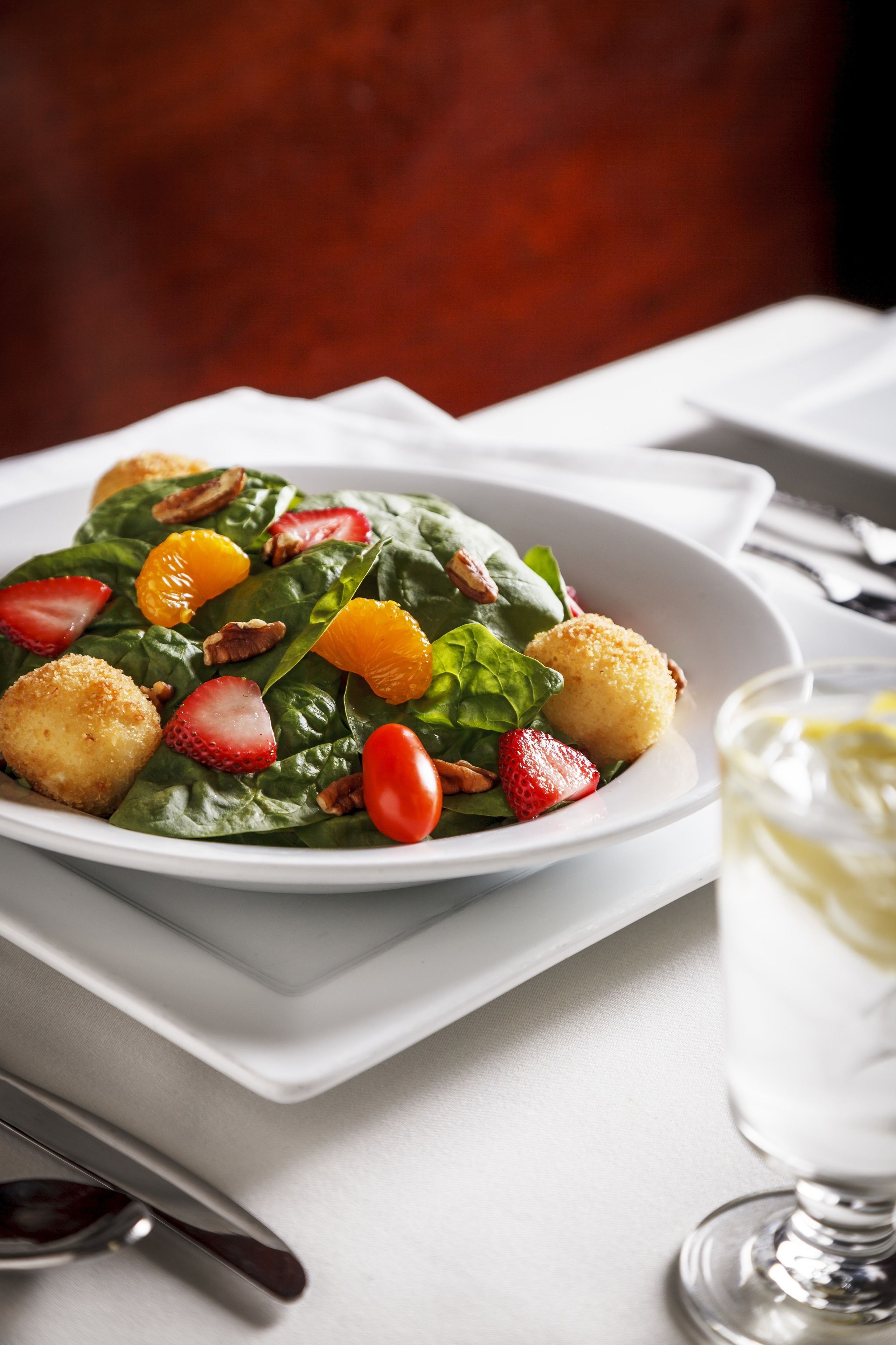 Un piatto bianco con un'insalata di spinaci, fragole e fettine d'arancia, accompagnato da un bicchiere di vino bianco.