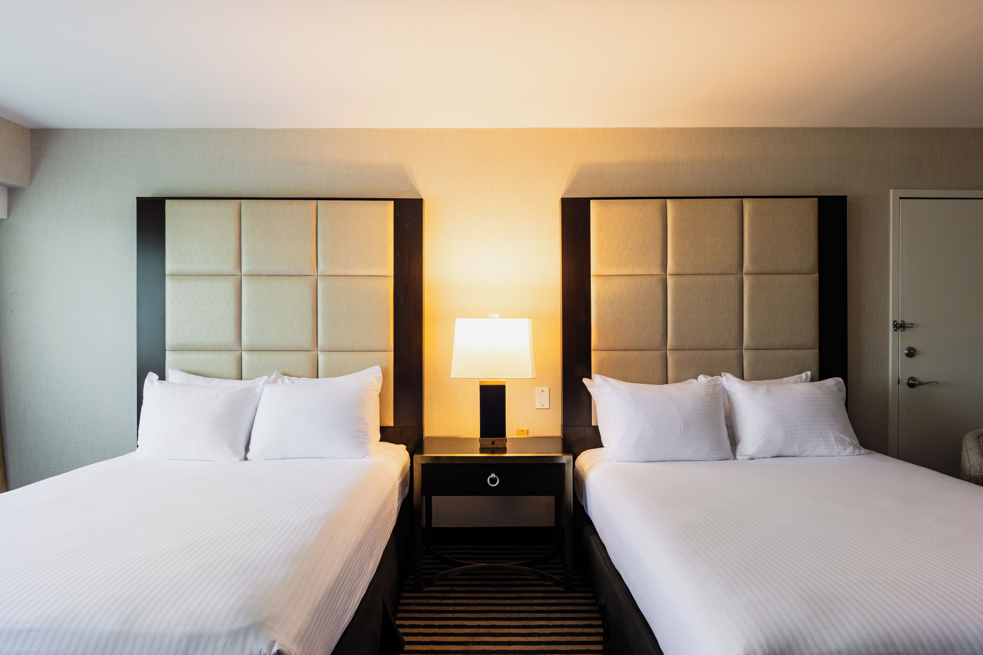 Ein Hotelzimmer mit zwei Betten, einem Nachttisch mit Lampe und einer Tür.