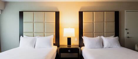 A hotel room with two beds, a nightstand with a lamp, and a door.