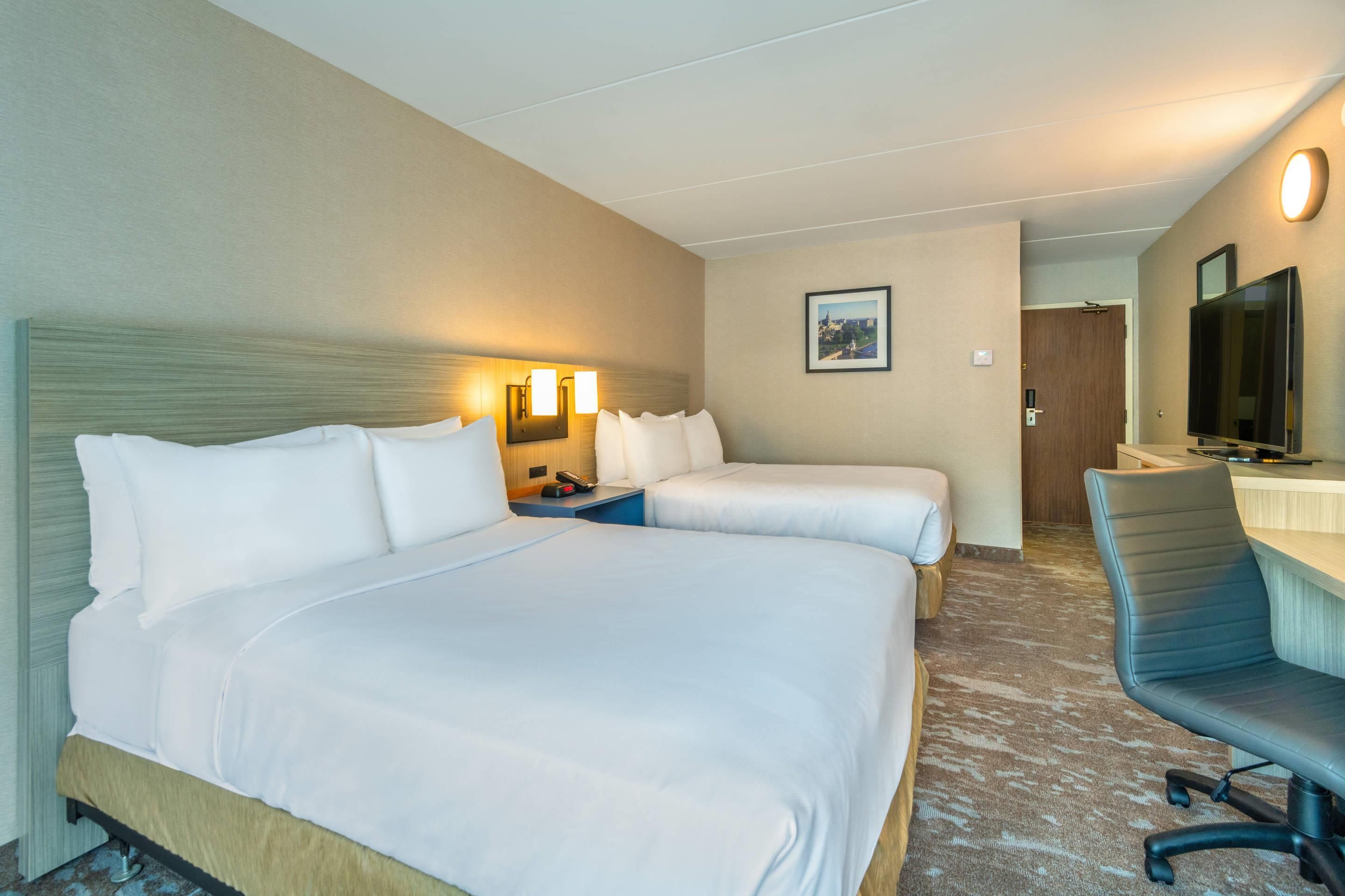 Una habitación de hotel con una cama grande, un escritorio con una silla, un televisor y un cuadro en la pared.