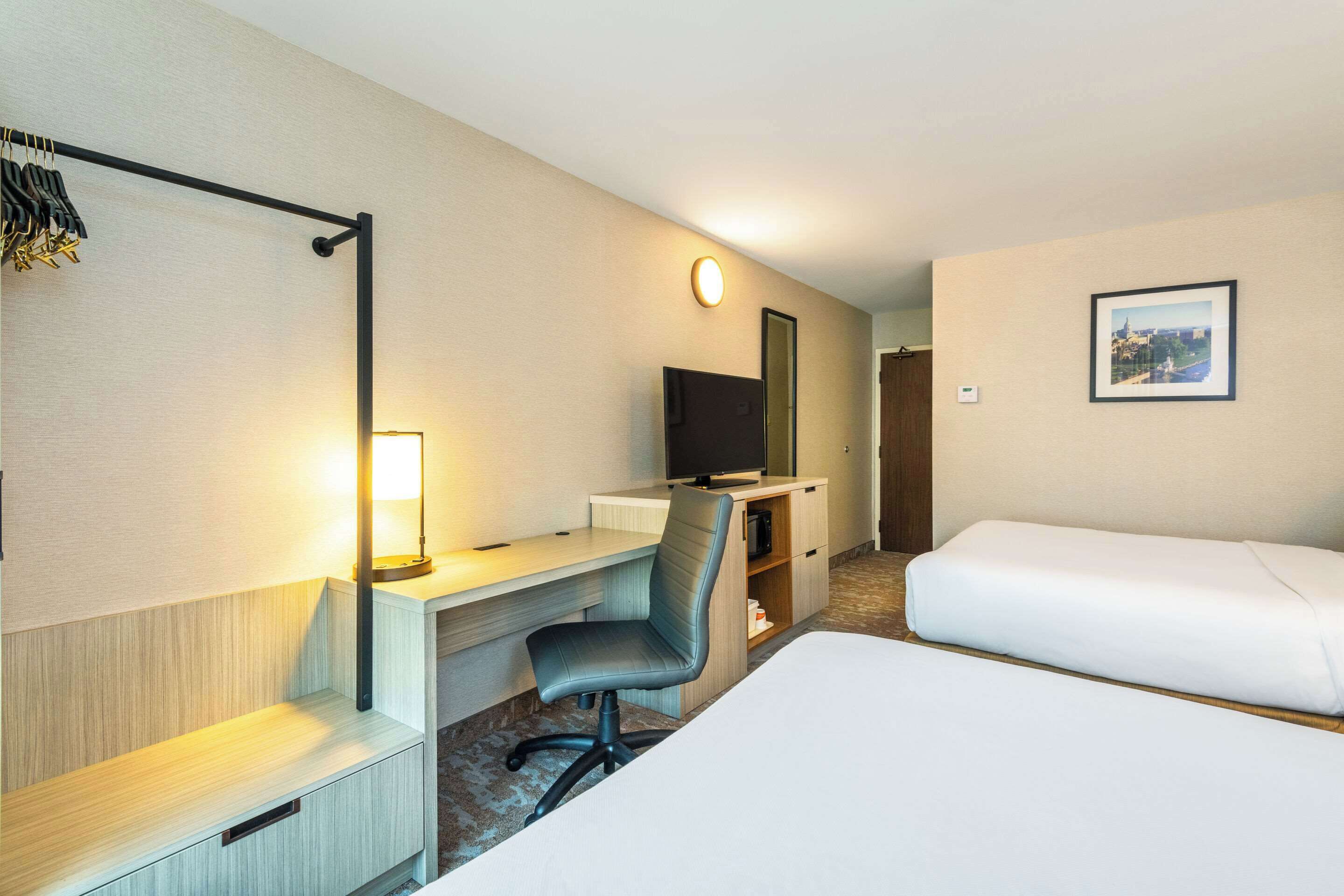 Ett hotellrum med ett skrivbord, en stol, en tv och två sängar.
