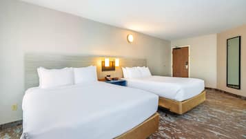 A hotel room with two beds, a nightstand, a wall-mounted light, and a door.