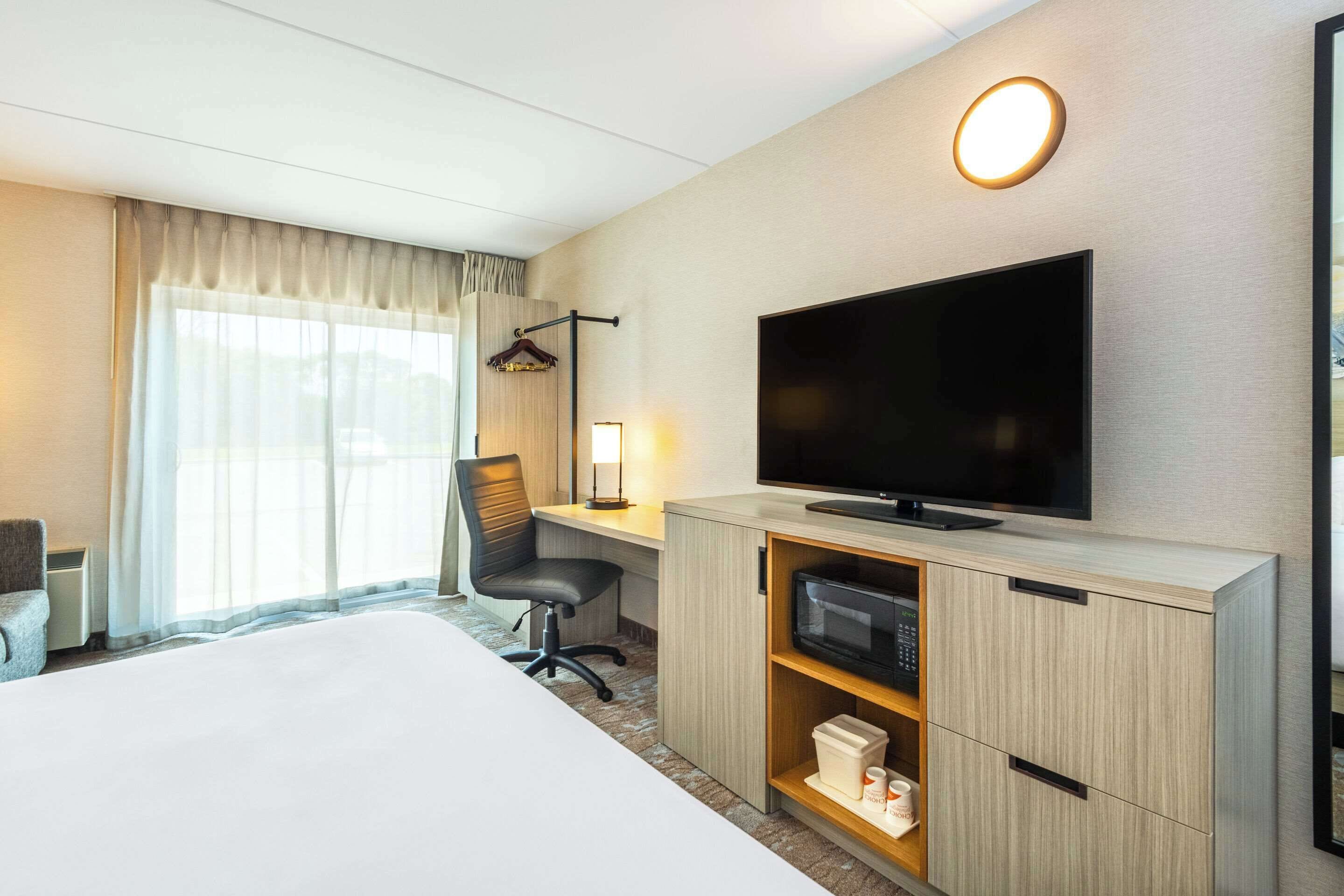 Une chambre d’hôtel comprenant un lit, un bureau avec une télévision, une chaise, une lampe de bureau et une armoire.