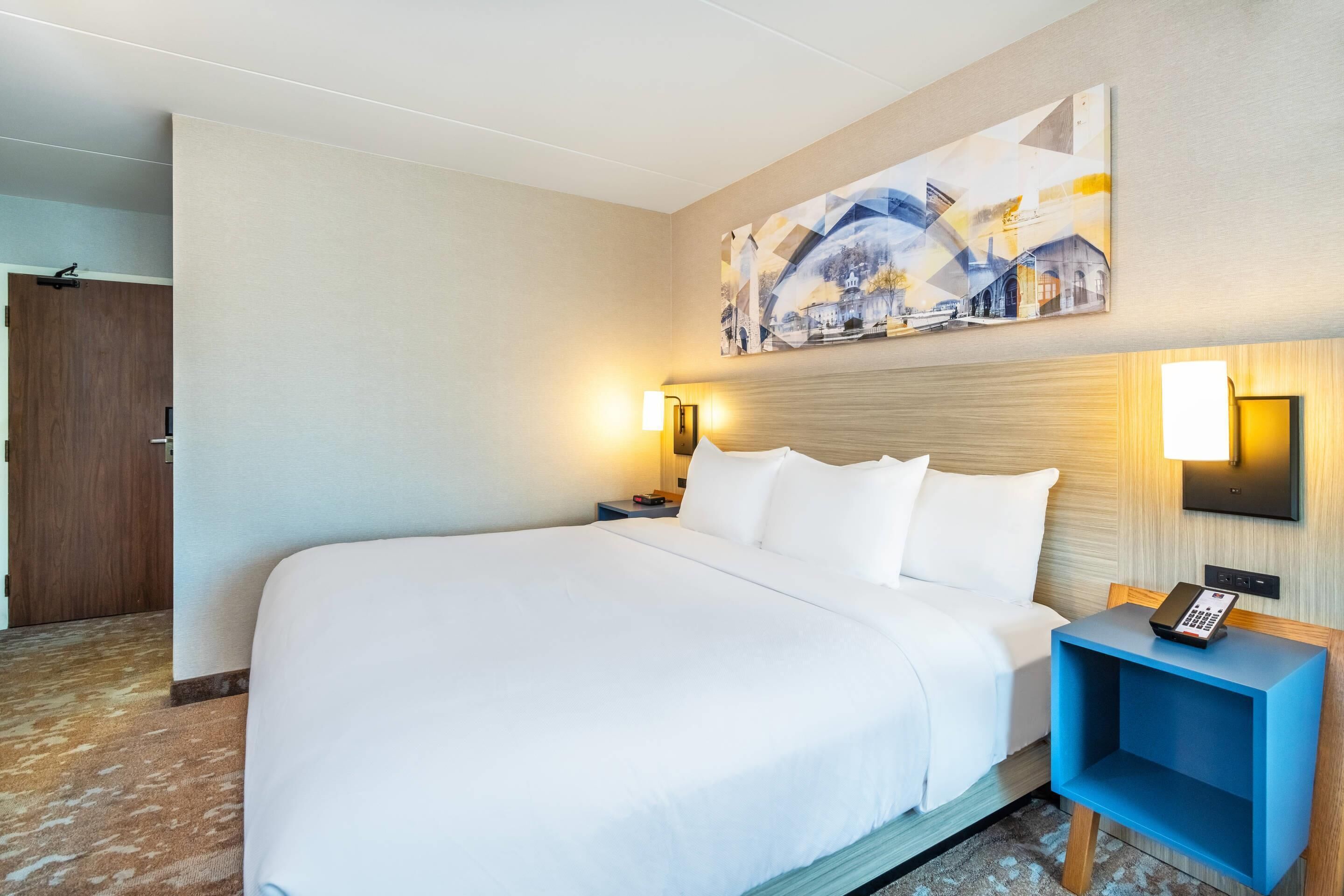 A hotel room with a large bed, a nightstand with a phone, and a wall-mounted light.