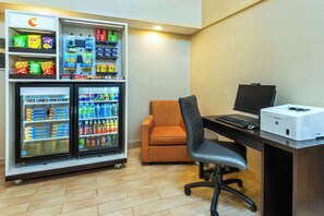 Una habitación de hotel con minibar, un escritorio con computadora y una silla estampada color naranja.