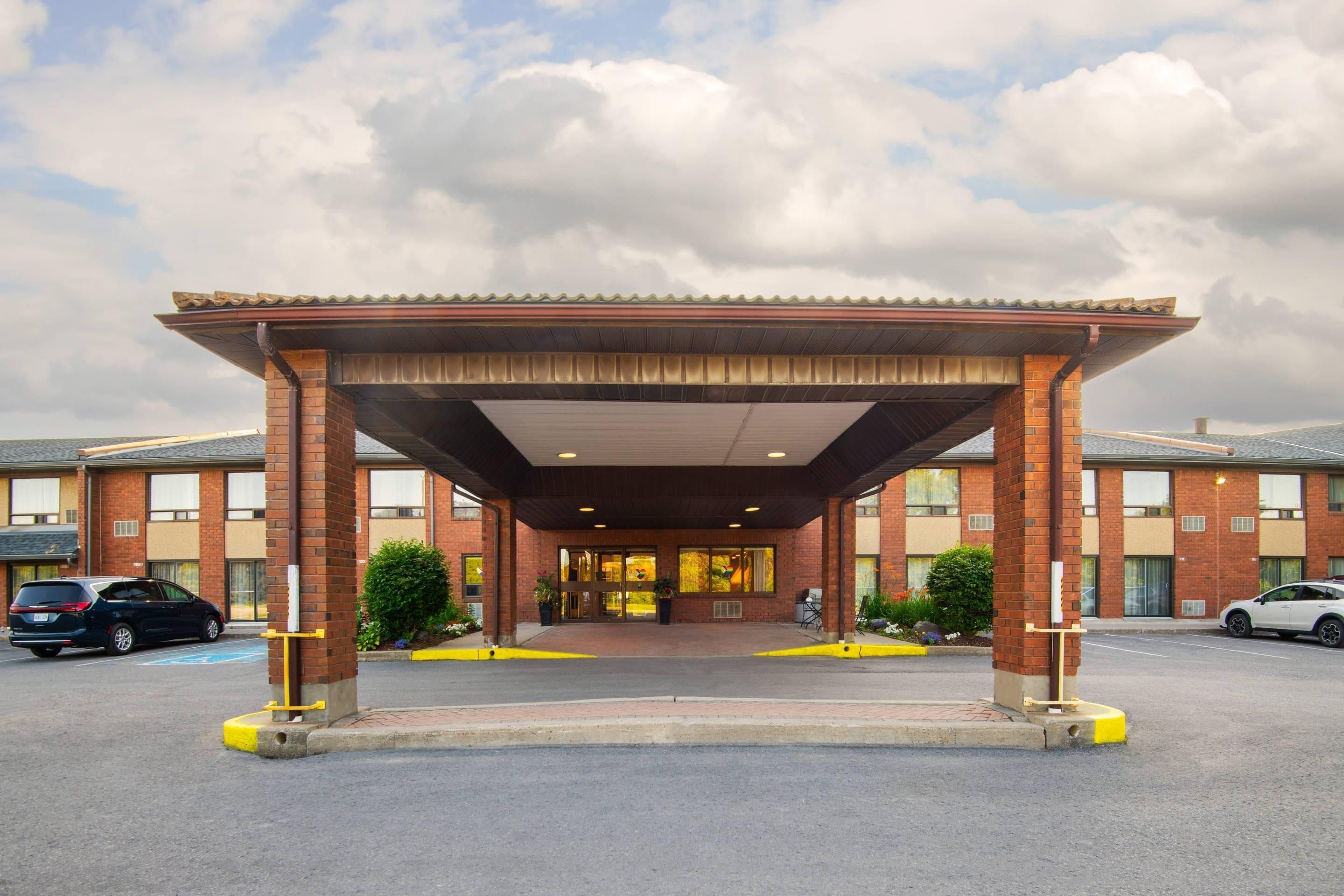 A hotel entrance with a covered walkway, brick facade, and a parking lot.