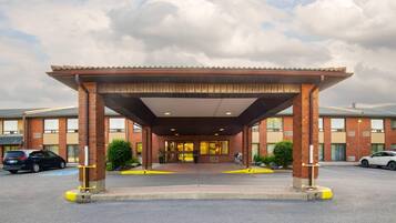 A hotel entrance with a covered walkway, brick facade, and a parking lot.