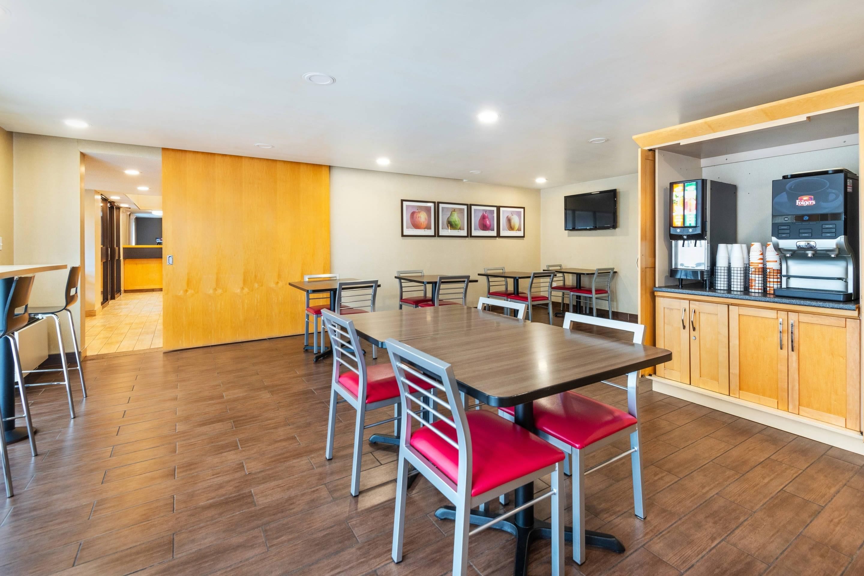 Un espace repas moderne avec plusieurs tables et chaises, un coin cuisine équipé d’une machine à café et des œuvres d’art encadrées accrochées au mur.