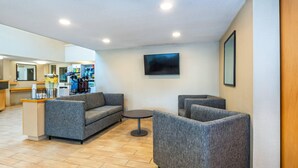 Eine Lobby mit grau gepolsterten Sofas, einem kleinen runden Tisch, einem an der Wand montierten Flachbildfernseher und einer Rezeption mit Theke.