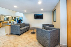 A lobby with grey upholstered sofas, a small round table, a flat-screen TV mounted on the wall, and a reception desk with a counter. - Comfort Inn Kingston - Highway 401 (Kingston)