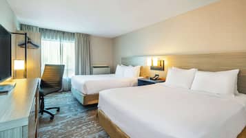 A hotel room with two beds, a desk, a chair, a TV, and a window with curtains.