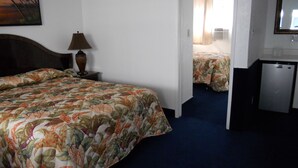 A hotel room with a bed, a desk, a lamp, and a door leading to another room. - Los Angeles Adventurer All Suite Hotel at LAX (Inglewood)