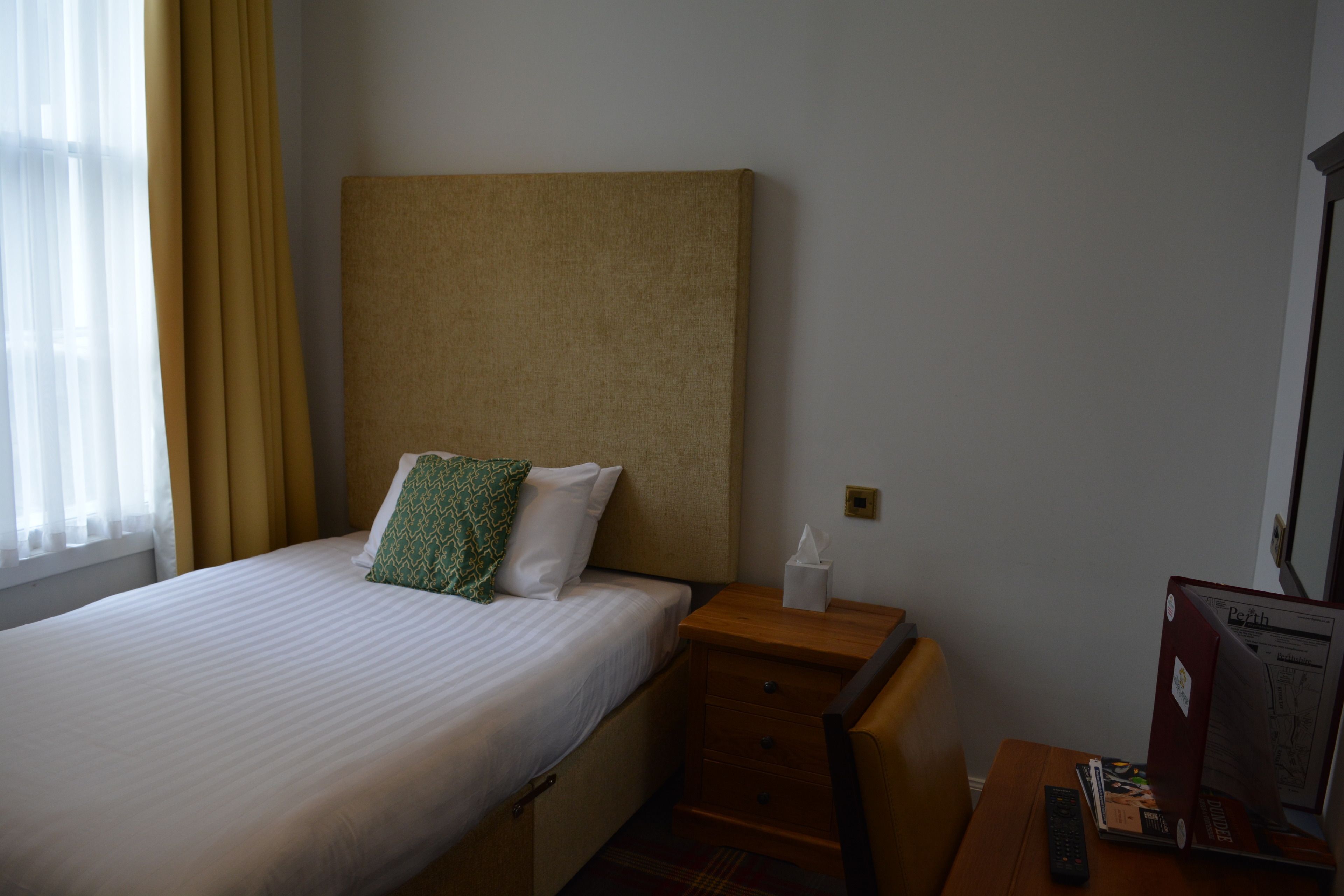 Una habitación de hotel con una cama, una mesita de noche, un escritorio y una computadora.