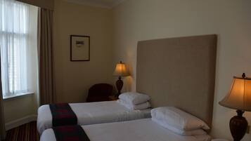A hotel room with two beds, a nightstand with a lamp, a chair, and a framed picture on the wall.