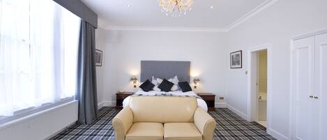 Une chambre d’hôtel avec un grand lit, un canapé, une table ronde et un lustre.