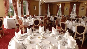 A banquet hall with round tables set for a formal event, featuring white tablecloths, silverware, and red upholstered chairs. - The Royal George Hotel (Perth)