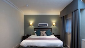 A neatly made bed with a headboard, two bedside lamps, a nightstand, and a plaid-patterned floor. - The Royal George Hotel (Perth)