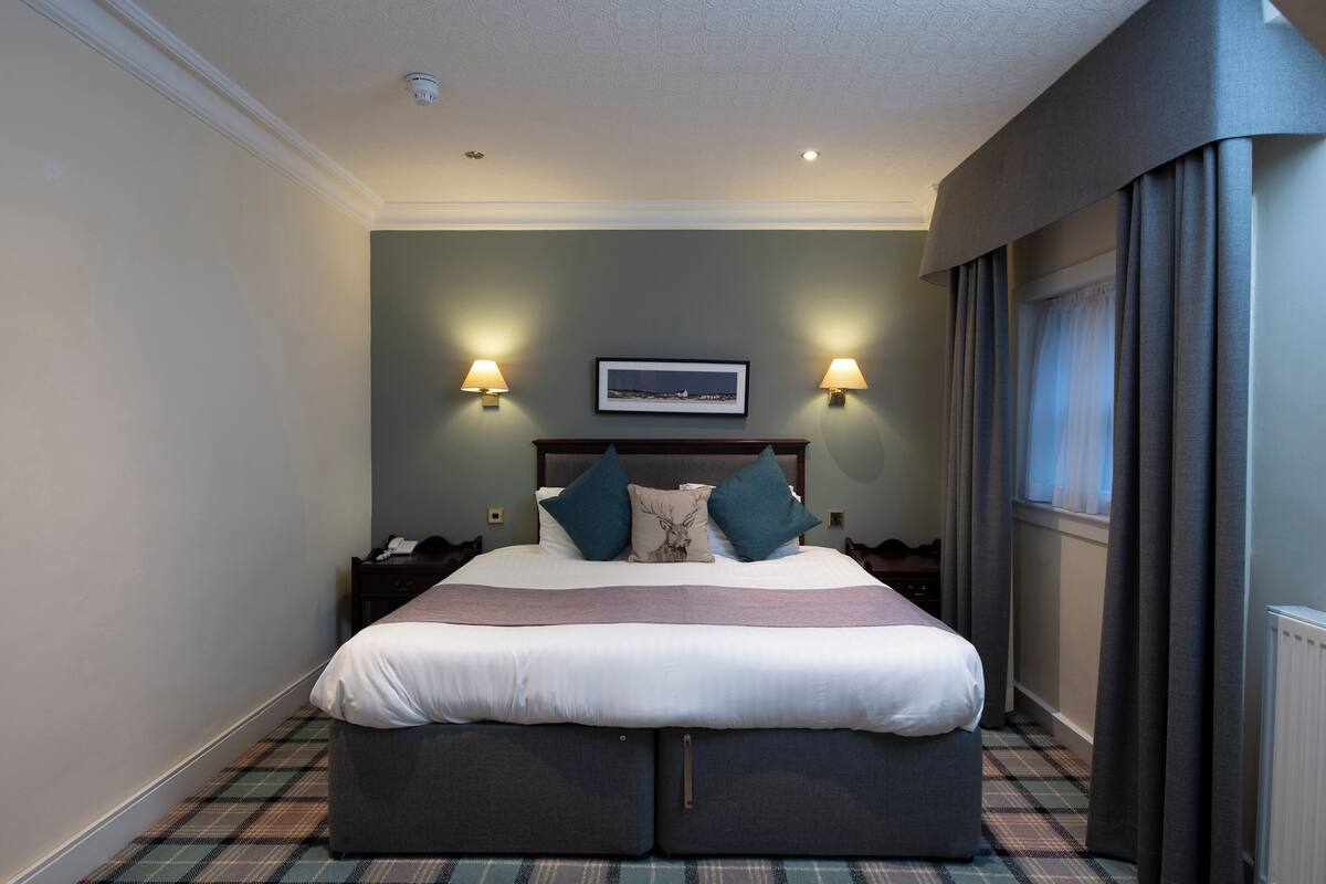 A neatly made bed with a headboard, two bedside lamps, a nightstand, and a plaid-patterned floor.