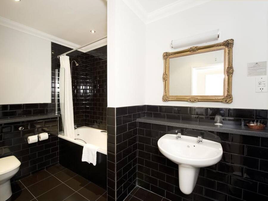 Un baño con diseño de baldosas blanco y negro, un lavabo blanco, una bañera y un espejo con marco dorado.