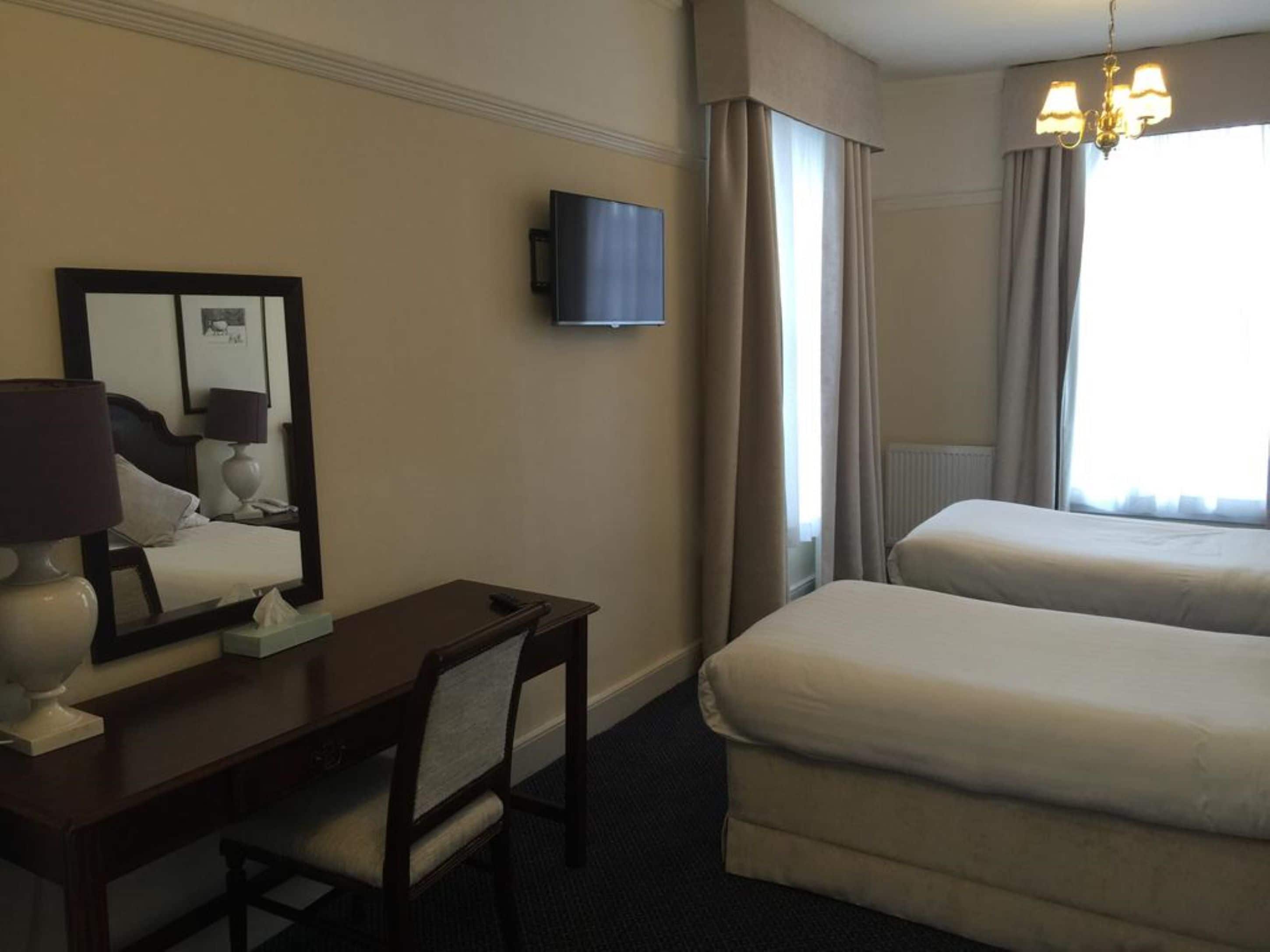 Hotellihuone, jossa on työpöytä, tuoli, kaksi sänkyä, televisio ja kattokruunu.