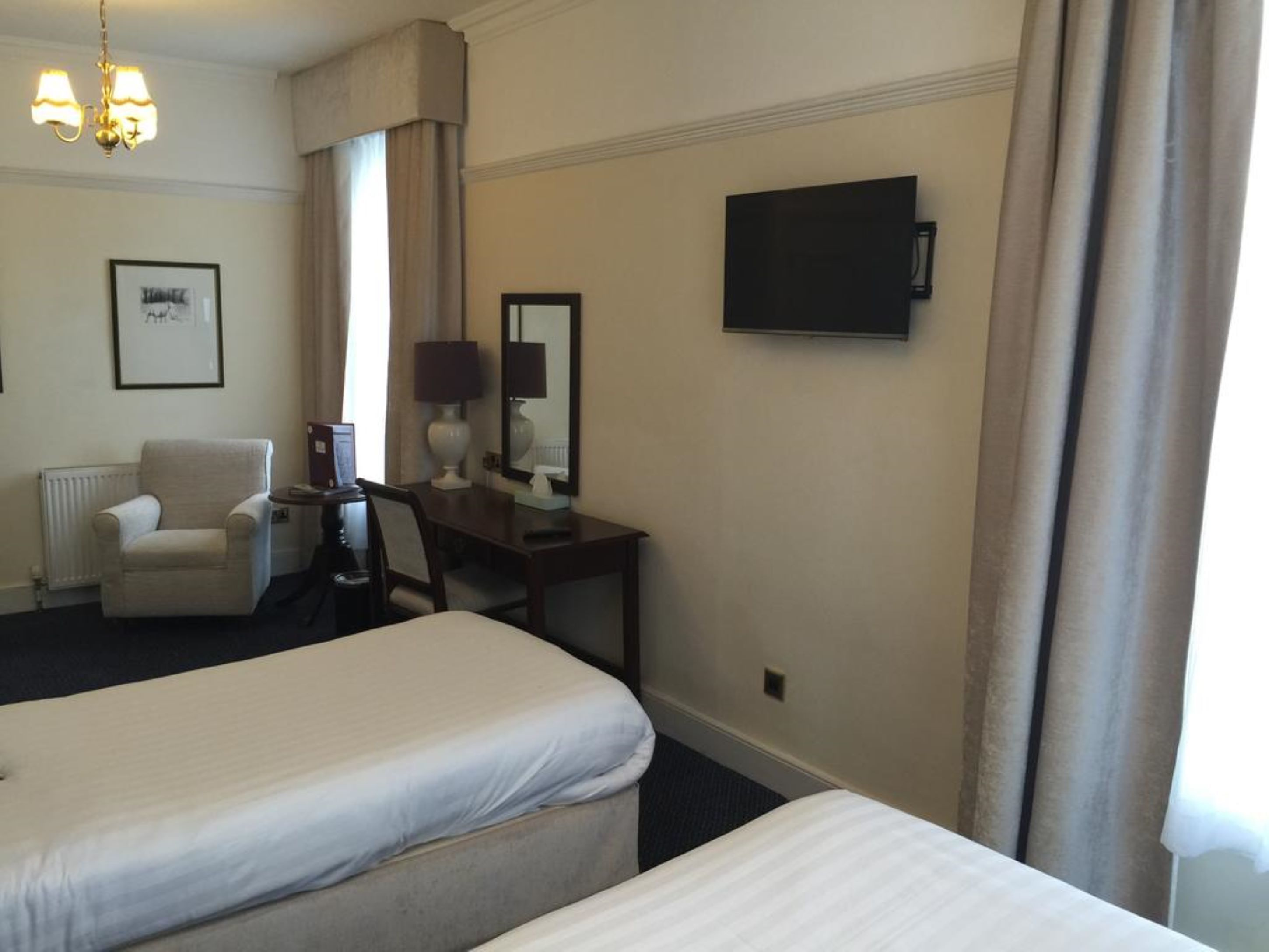 A hotel room with two beds, a desk, a chair, a lamp, a television, and a framed picture on the wall.