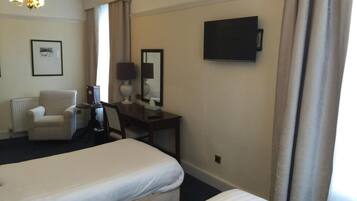 Quarto de hotel com duas camas, uma escrivaninha, uma cadeira, um abajur, uma televisão e um quadro na parede.