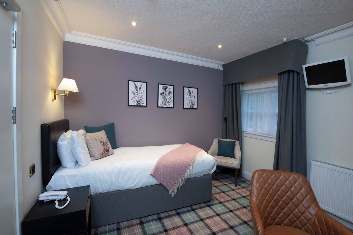 A hotel room with a bed, a chair, a TV, and a lamp.